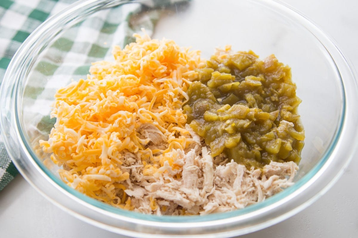This chicken enchilada recipe is bursting with flavor and perfect for busy nights. Plus, it's freezer-friendly! Ingredients for chicken enchiladas - Chicken, cheese, and green chilies mixed in a glass bowl.