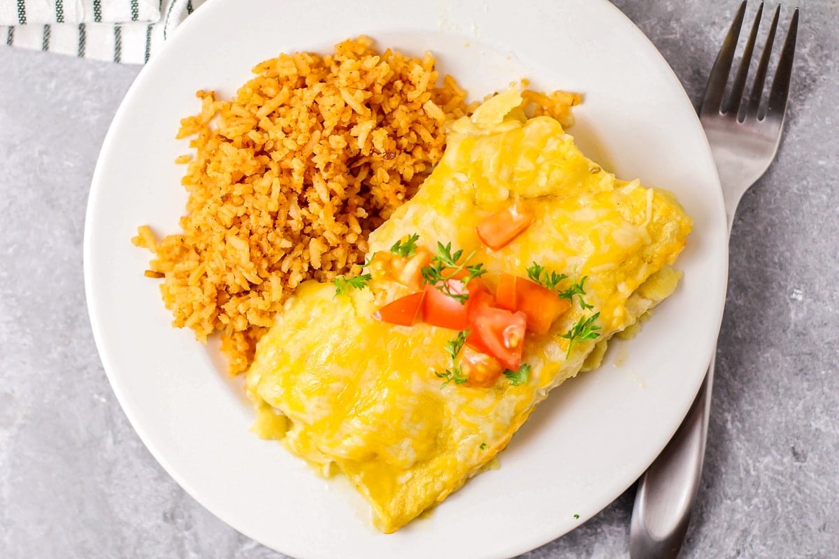This chicken enchilada recipe is bursting with flavor and perfect for busy nights. Plus, it's freezer-friendly! Close up image of our green chili chicken enchilada recipe on white plate.