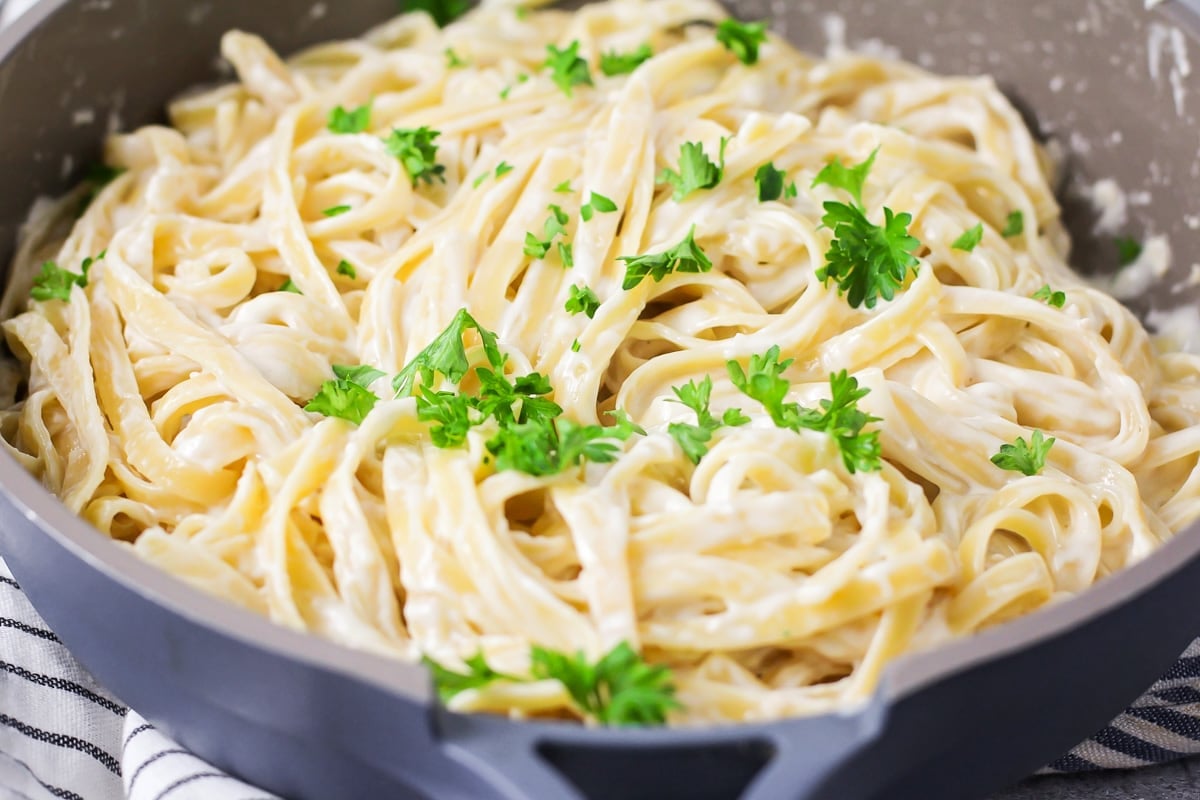 Indulge in the rich and comforting flavors of this Fettuccine Alfredo recipe that's on the table in only 30 minutes! Fresh parsley sprinkled over easy Fettuccine Alfredo in skillet.