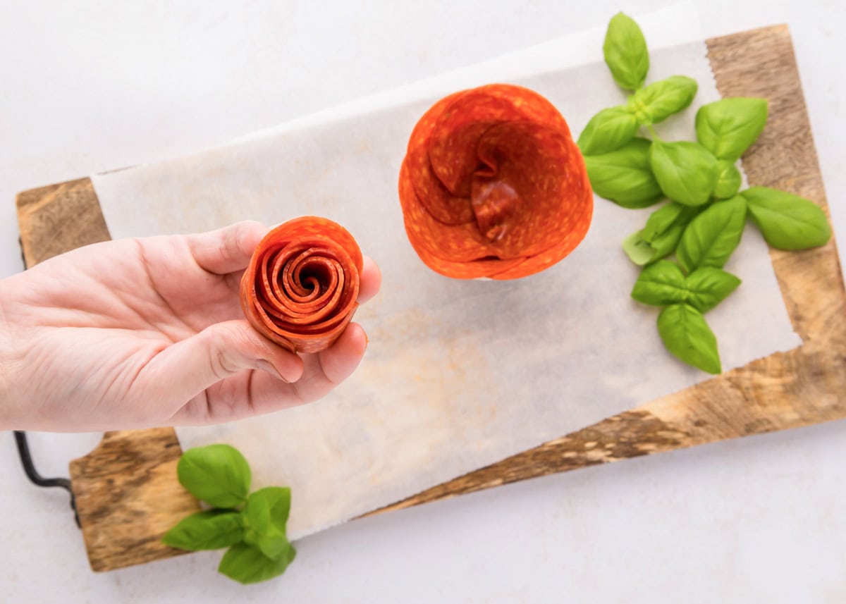 Pepperoni roses are a fun and easy way to elevate your charcuterie board, adding a beautiful and delicious touch. Rolling and placing a rolled pepperoni into a glass jar.