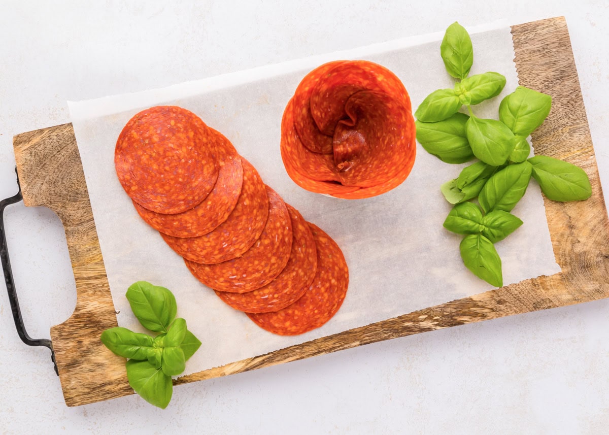 Pepperoni roses are a fun and easy way to elevate your charcuterie board, adding a beautiful and delicious touch. Pushing pepperoni into the glass jar.