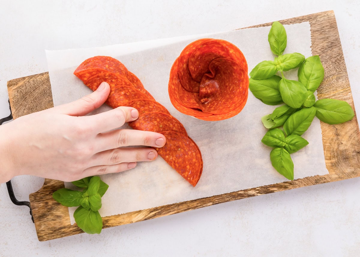 Pepperoni roses are a fun and easy way to elevate your charcuterie board, adding a beautiful and delicious touch. Layering, folding, and pushing pepperoni into a glass jar.