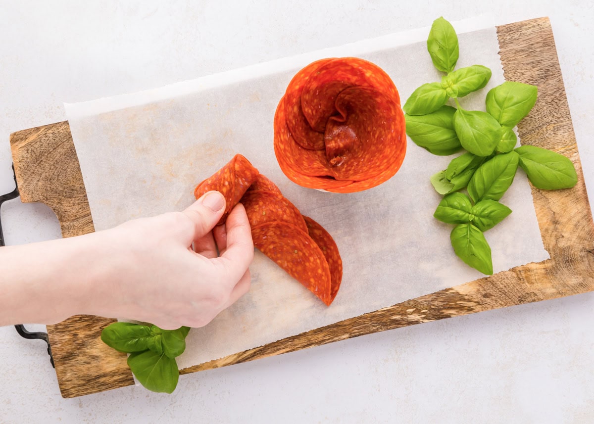 Pepperoni roses are a fun and easy way to elevate your charcuterie board, adding a beautiful and delicious touch. Folding and rolling pepperoni to place in a glass jar.