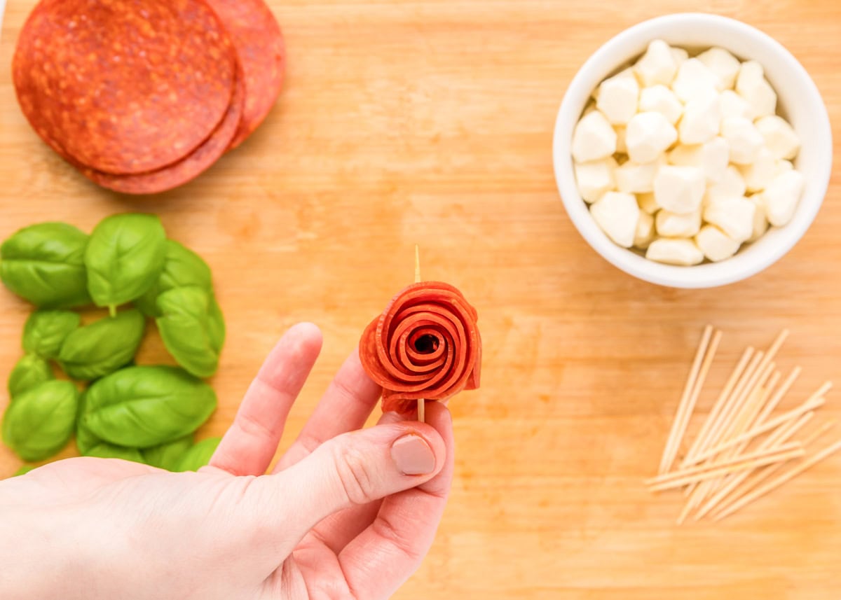 Create beautiful {and delicious} pepperoni rose skewers with only 3 ingredients and a few simple steps - a picture-perfect appetizer! Pushing a skewer through a rolled pepperoni flower.