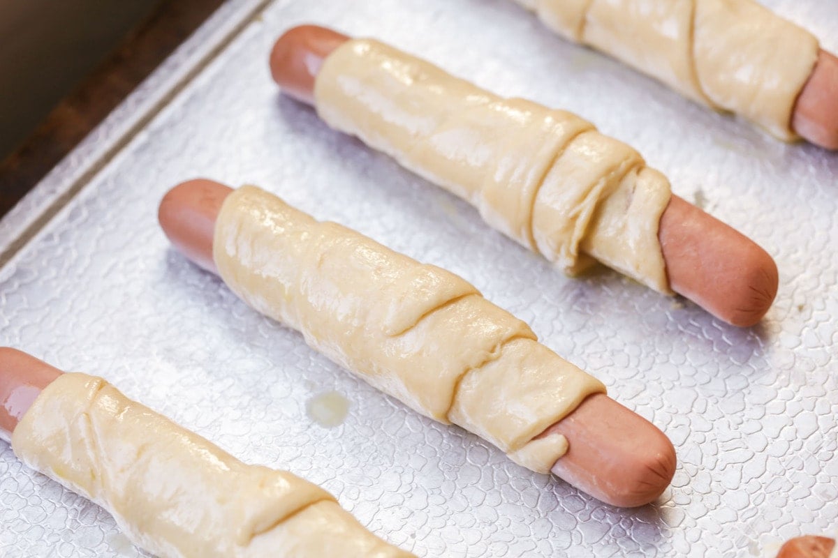 Both kids and adults will love these quick and simple pigs in a blanket. This nostalgic recipe is on the table in 20 minutes! Hot dogs wrapped in crescent dough and placed on a baking sheet.