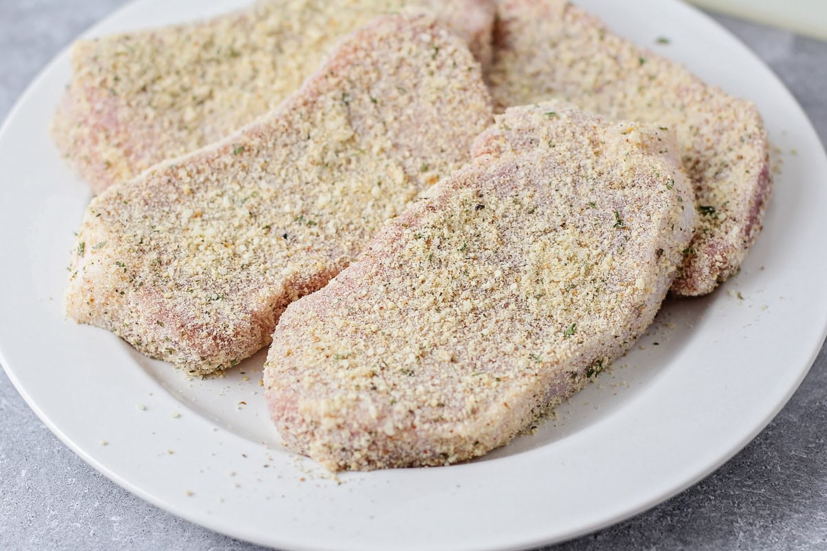 Crusted with parmesan and fried up with less than 10 minutes of prep work, this is definitely the best pork chop recipe you'll ever try!! Pork chops with a parmesan crust on a white plate.