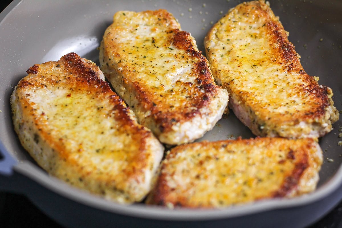 Crusted with parmesan and fried up with less than 10 minutes of prep work, this is definitely the best pork chop recipe you'll ever try!! Pork chops with a parmesan crust cooking in skillet.